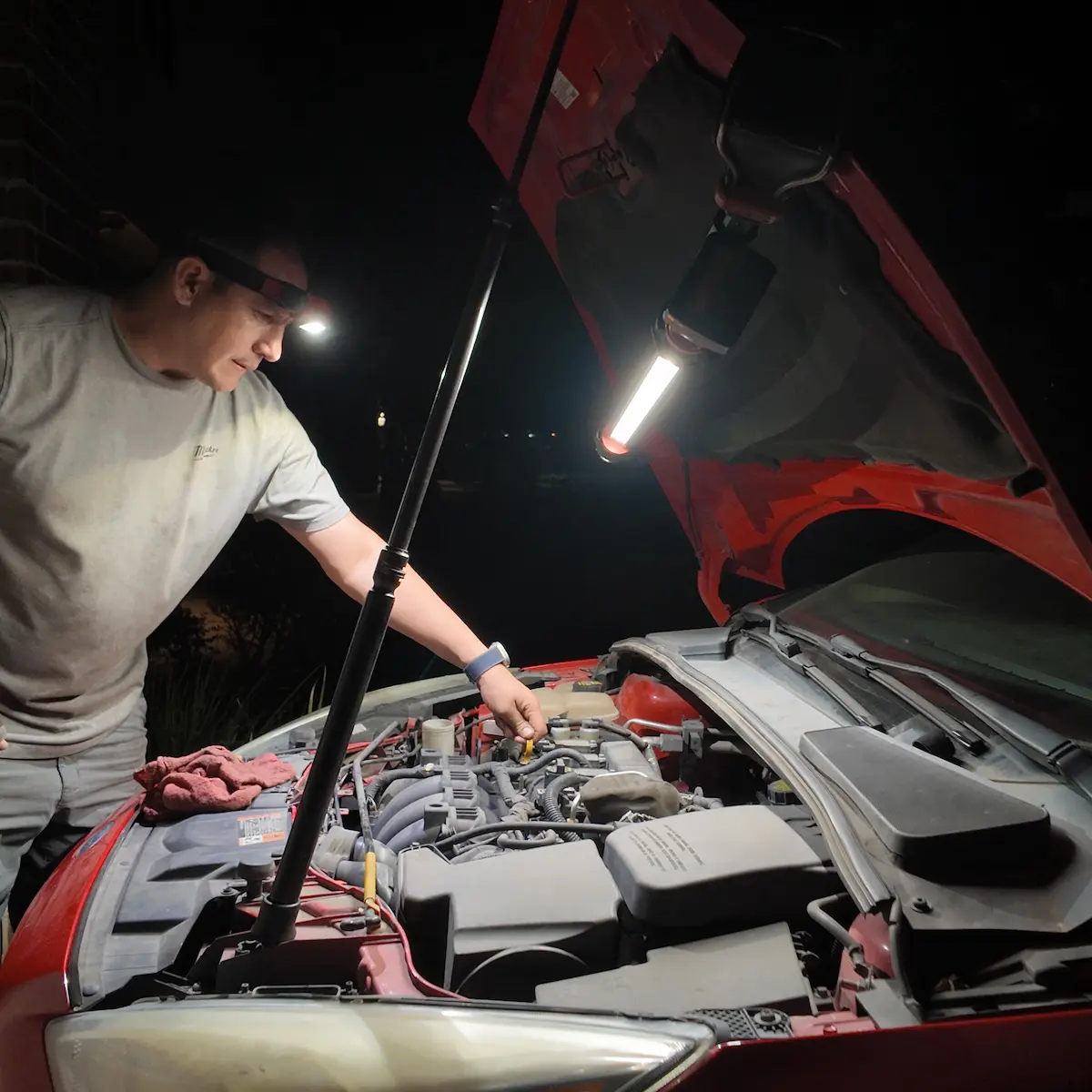 Martin checking under the hood of a car at night with a work light